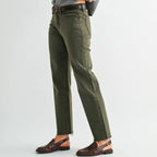 A woman modeling olive green straight-leg jeans with a black belt, styled with a gray knit sweater and brown leather loafers against a light gray studio background.