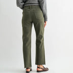 A woman is shown from behind wearing olive green straight-leg jeans, a gray knit sweater, and brown flat sandals against a light gray studio background.