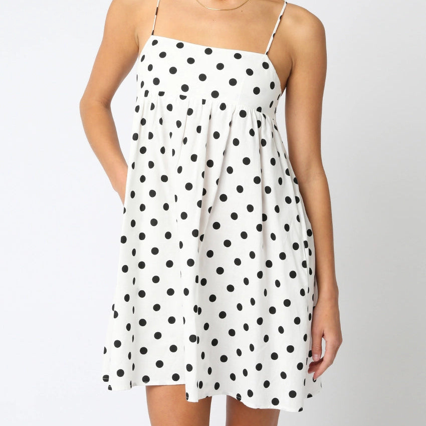 Woman wearing a white dress with black polka dots against a plain background