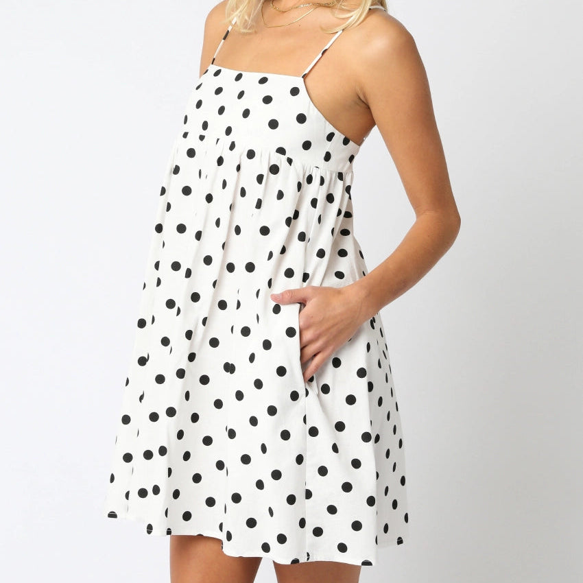 Woman wearing a white dress with black polka dots on a plain background