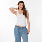 Woman wearing white ribbed square neck tank top with light blue drawstring denim pants against white background