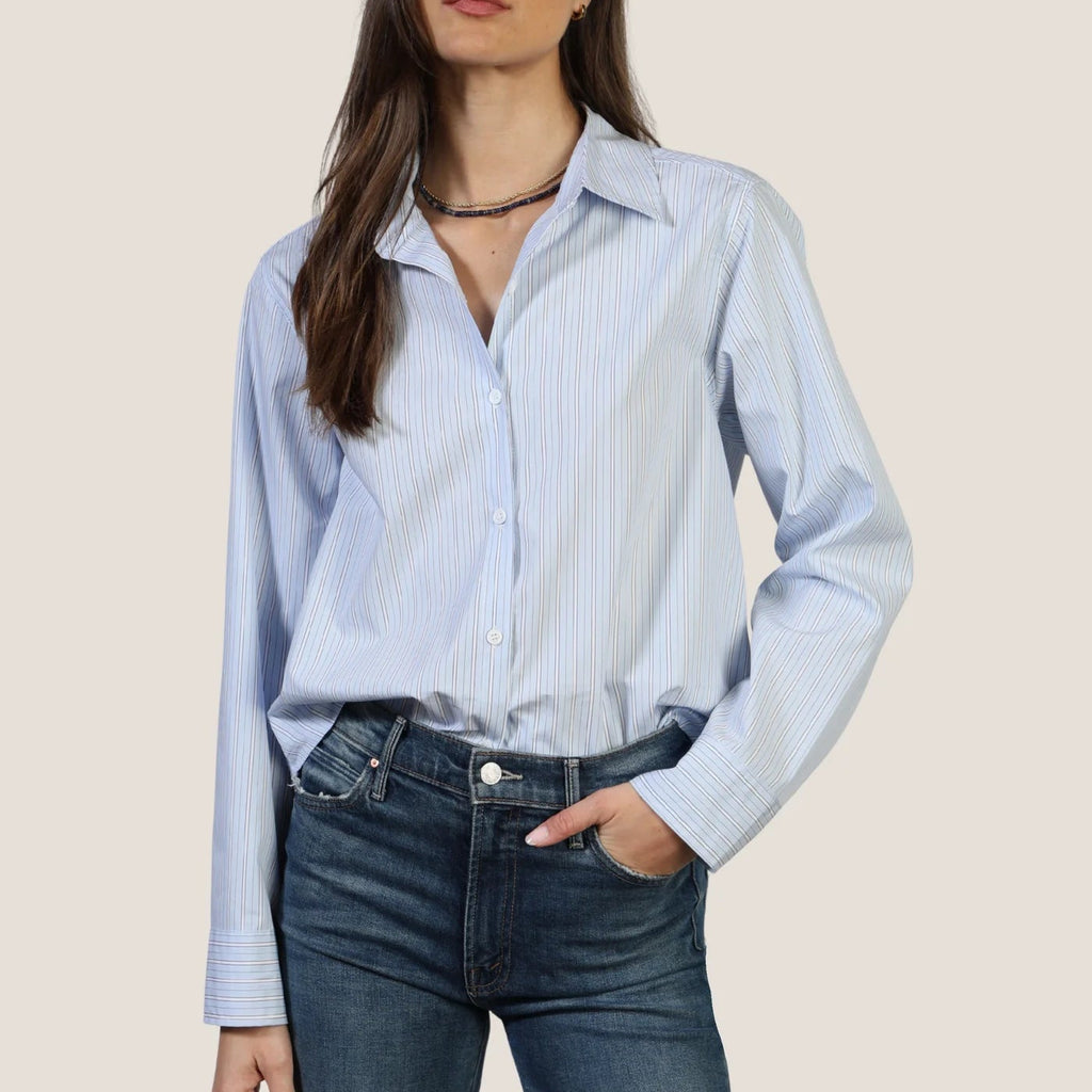 Woman wearing light blue striped button-up Hi-Lo Modern Shirt with dark jeans and beaded choker necklace