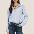 Woman wearing light blue striped button-up Hi-Lo Modern Shirt with dark jeans and beaded choker necklace