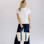 Woman in a white short sleeve top holding a woven bag with wavy pattern against a plain background
