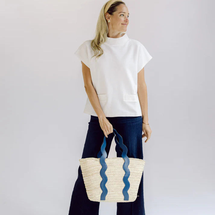 Woman in a white short sleeve top holding a woven bag with wavy pattern against a plain background