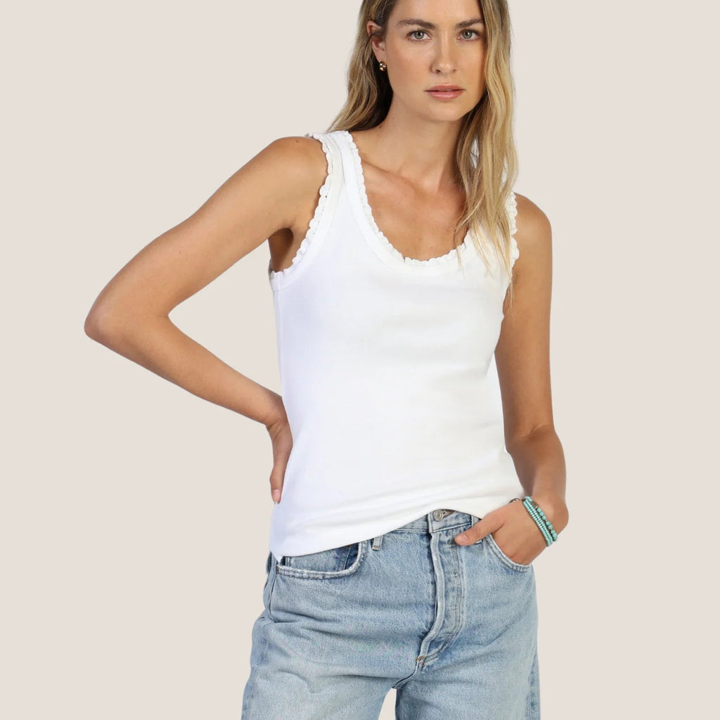 Woman wearing a white tank top and light blue denim shorts on a plain background