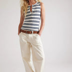 Woman wearing a striped sleeveless top and white pants on a plain background