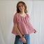 Woman wearing pink gingham Joey Blouse with short puffed sleeves and button front, styled with blue jeans