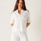 Woman wearing white Josephine Ruffle Henley Tee with half sleeves and button front, paired with white pants