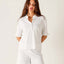 Woman wearing white Josephine Ruffle Henley Tee with half sleeves and button front, paired with white pants