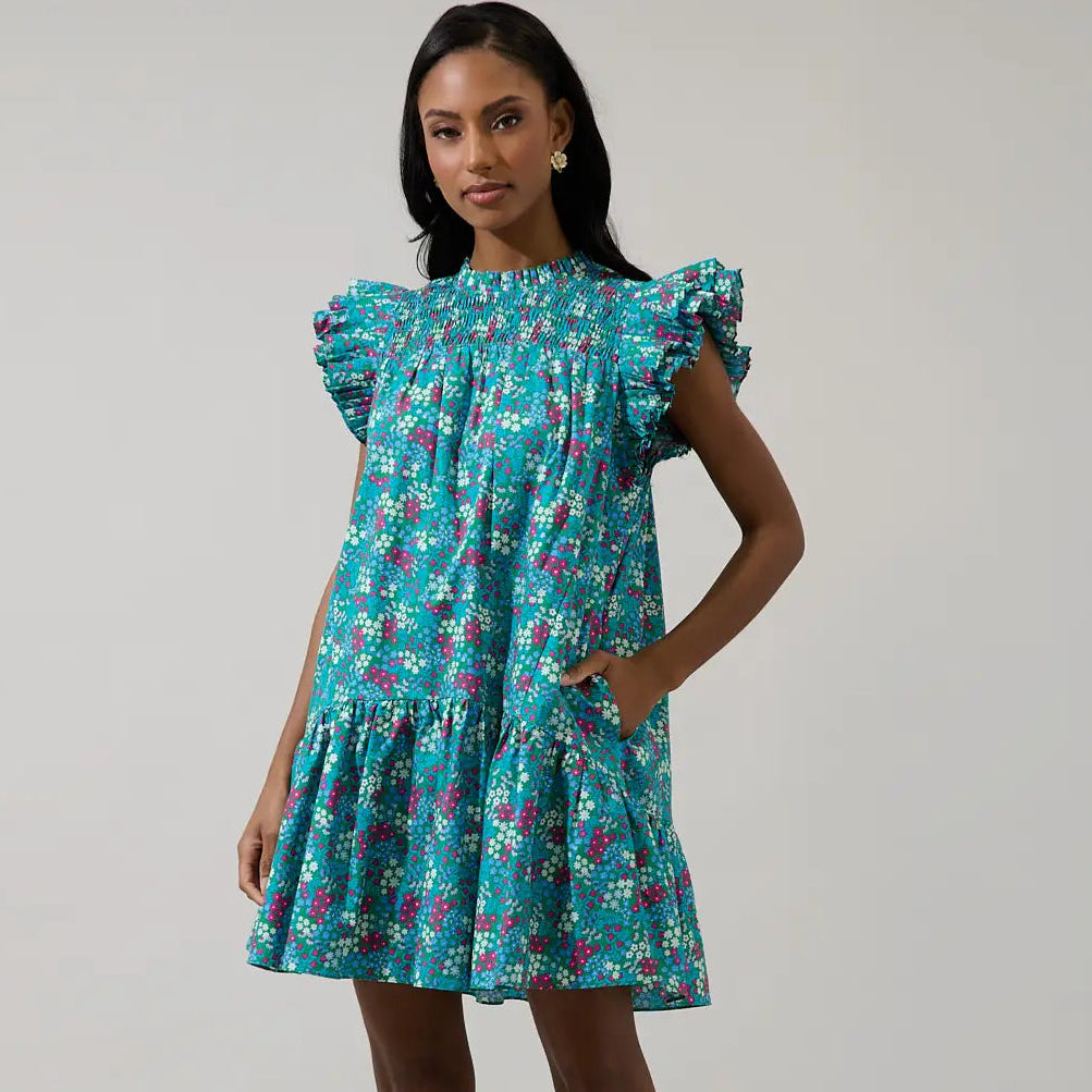 Woman wearing turquoise floral smocked mini dress with ruffled cap sleeves and tiered skirt