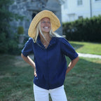 Woman wearing a straw hat and blue shirt outdoors with a house in the background