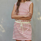 Woman wearing a red and white striped dress against a gray wall.