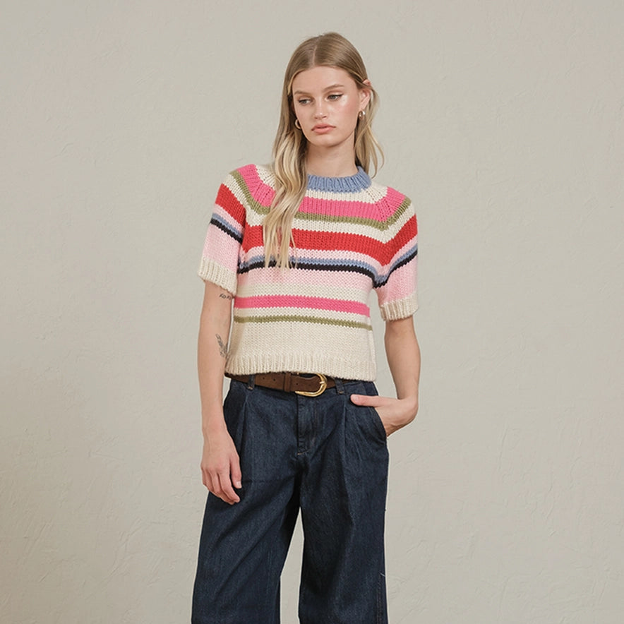 Woman wearing colorful striped short-sleeve knit sweater with pink, red, navy, and green horizontal stripes over dark denim … Main image