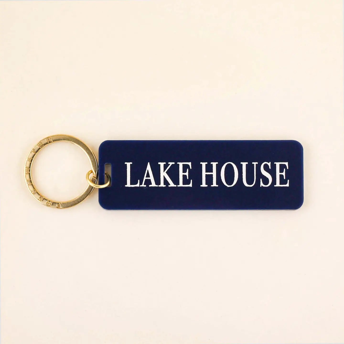Navy blue rectangle keychain with gold ring and white LAKE HOUSE text on cream background