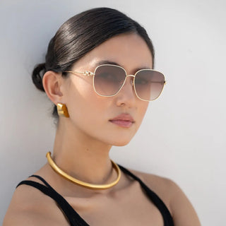 Woman wearing Lea Sunglasses with gold-tone metal frames and brown gradient lenses, paired with gold jewelry