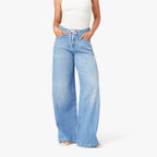 Woman wearing white tank top and light blue wide-leg drawstring jeans with white sneakers, hands in pockets