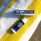 LipJao Lip Butter in navy blue tube with white cap, displayed on colorful striped textured fabric background
