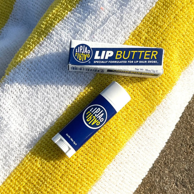 LipJao Lip Butter in navy blue tube with white cap, displayed on colorful striped textured fabric background Main image