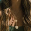Gold toggle necklace with two ornate star-shaped pendants, worn by woman with long brown hair and green sweater