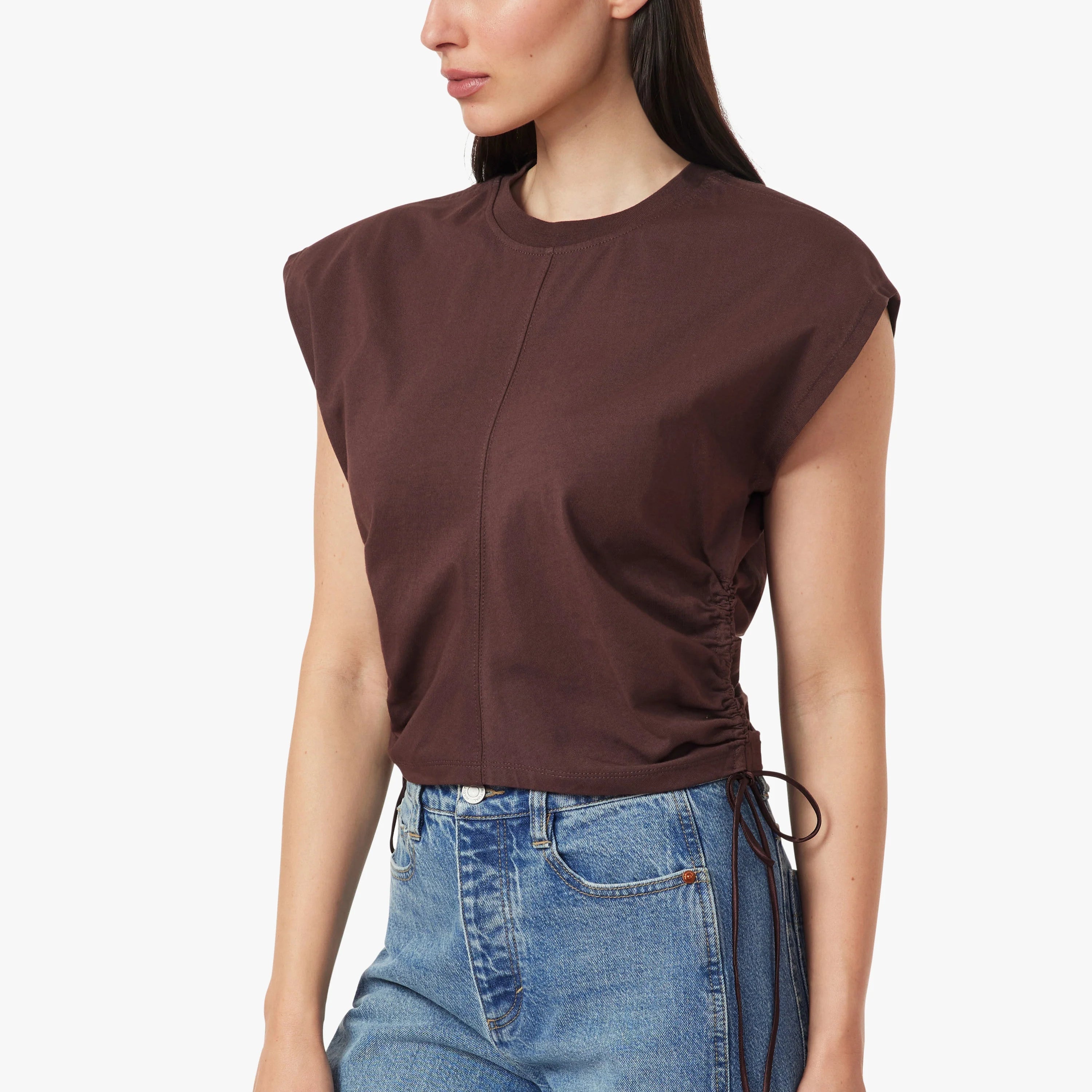 A woman modeling a dark brown sleeveless top with a gathered front and side drawstring, paired with blue jeans, against a plain white studio background. Main image