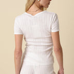 Woman wearing a white ribbed top and pants on a beige background