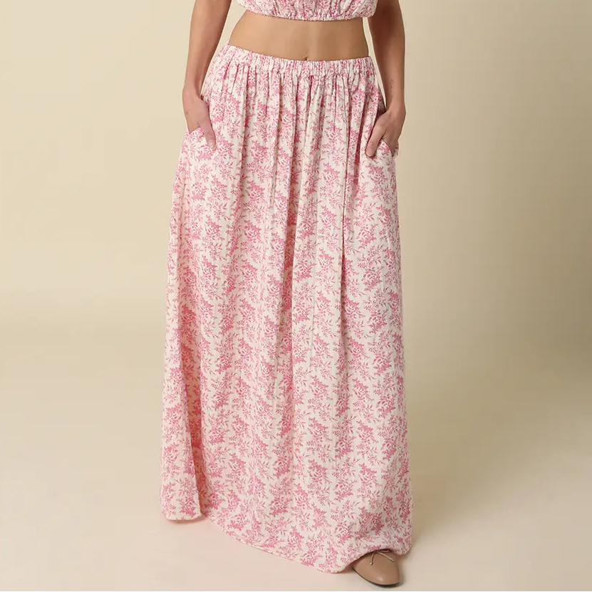 Woman wearing pink floral maxi skirt with elastic waistband and side pockets, paired with matching crop top