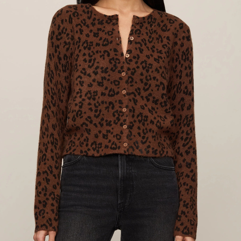 A woman modeling a brown long-sleeve button-front top with a black leopard print pattern, paired with dark jeans, against a plain light beige studio background.