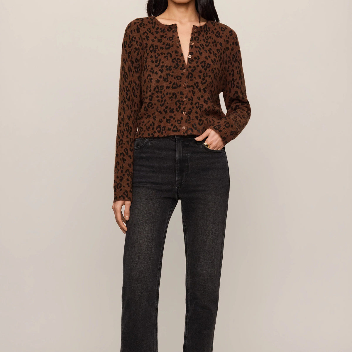A woman modeling a brown and black leopard-print long-sleeve top with black jeans and black pointed flats, standing against a plain light beige studio background.