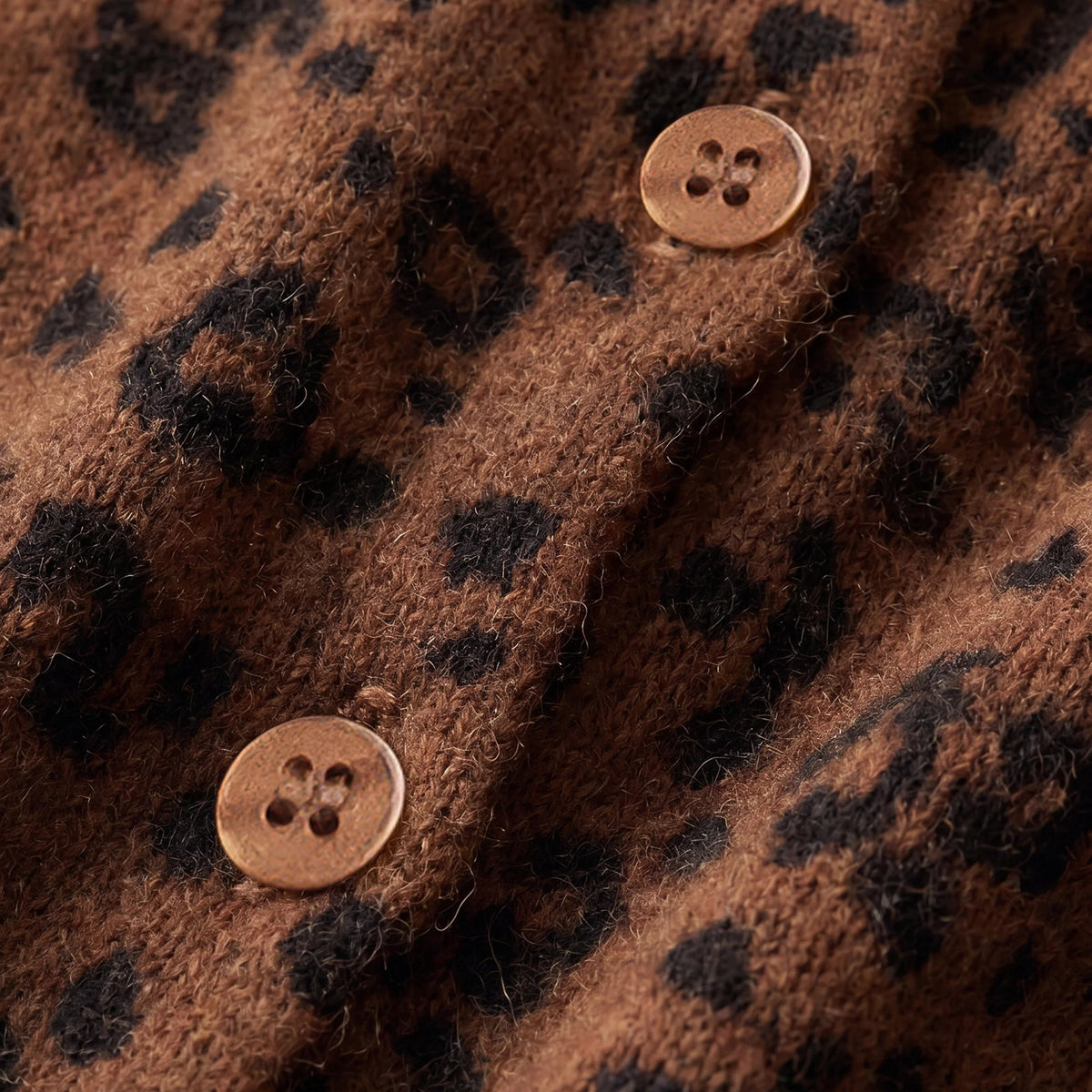 Close-up of a brown textured fabric with a black leopard print pattern and two round buttons.