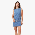 Woman wearing sleeveless light blue denim mini dress with studded belt cinched at waist