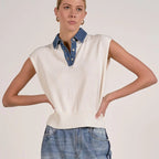 Woman wearing cream cap sleeve sweater top with denim collar over blue jeans, posing against neutral background