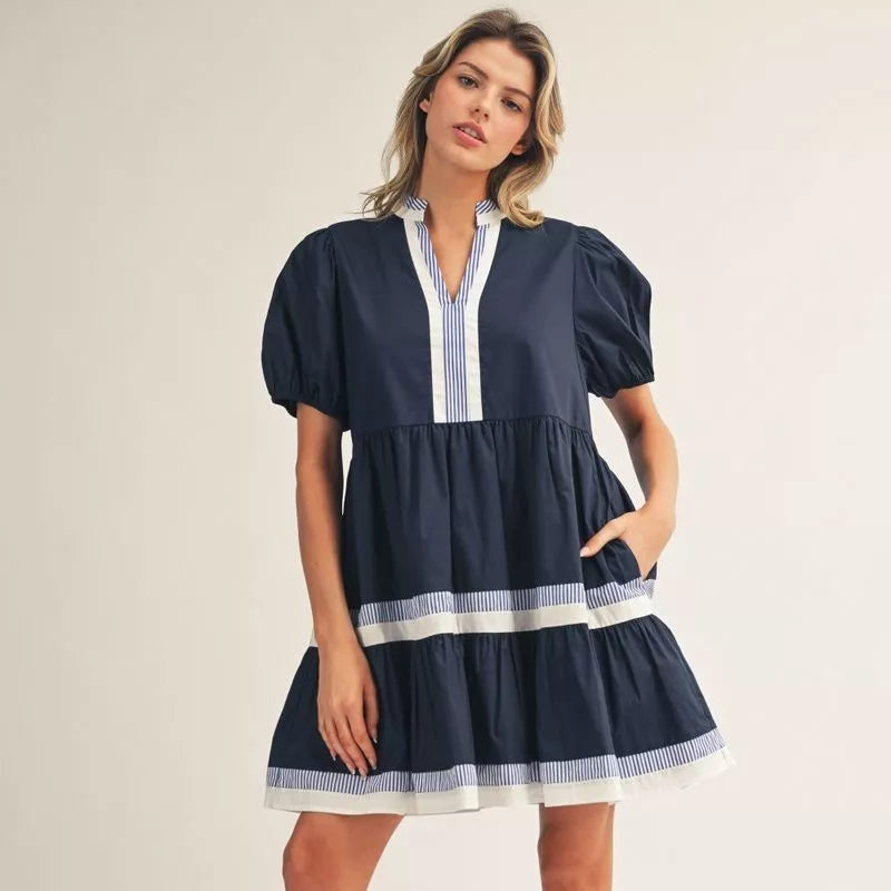 Navy blue women's dress with puffed sleeves, white striped front placket, and tiered skirt with white trim details Main image