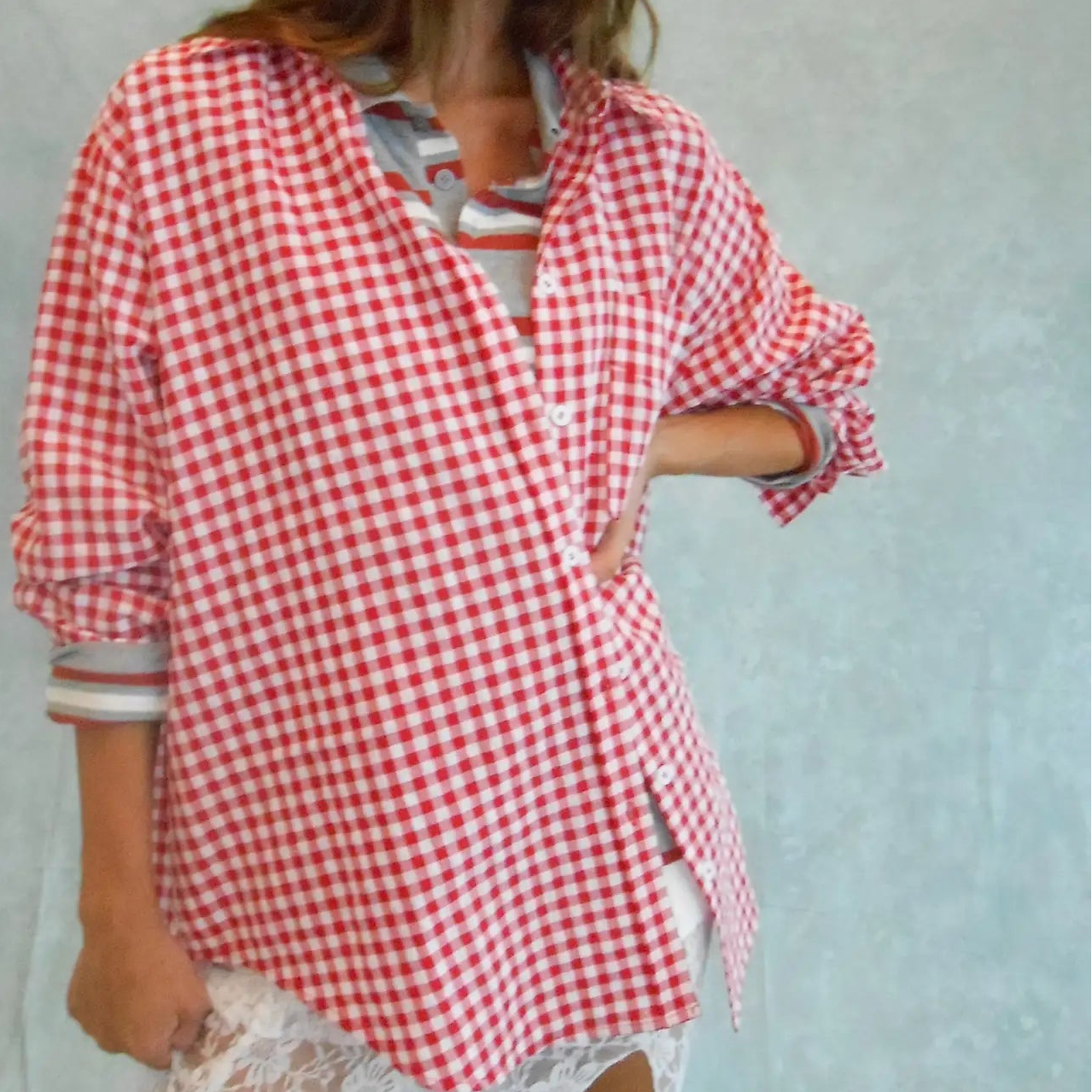 Woman wearing red and white gingham oversized button-down shirt with rolled sleeves over white distressed shorts