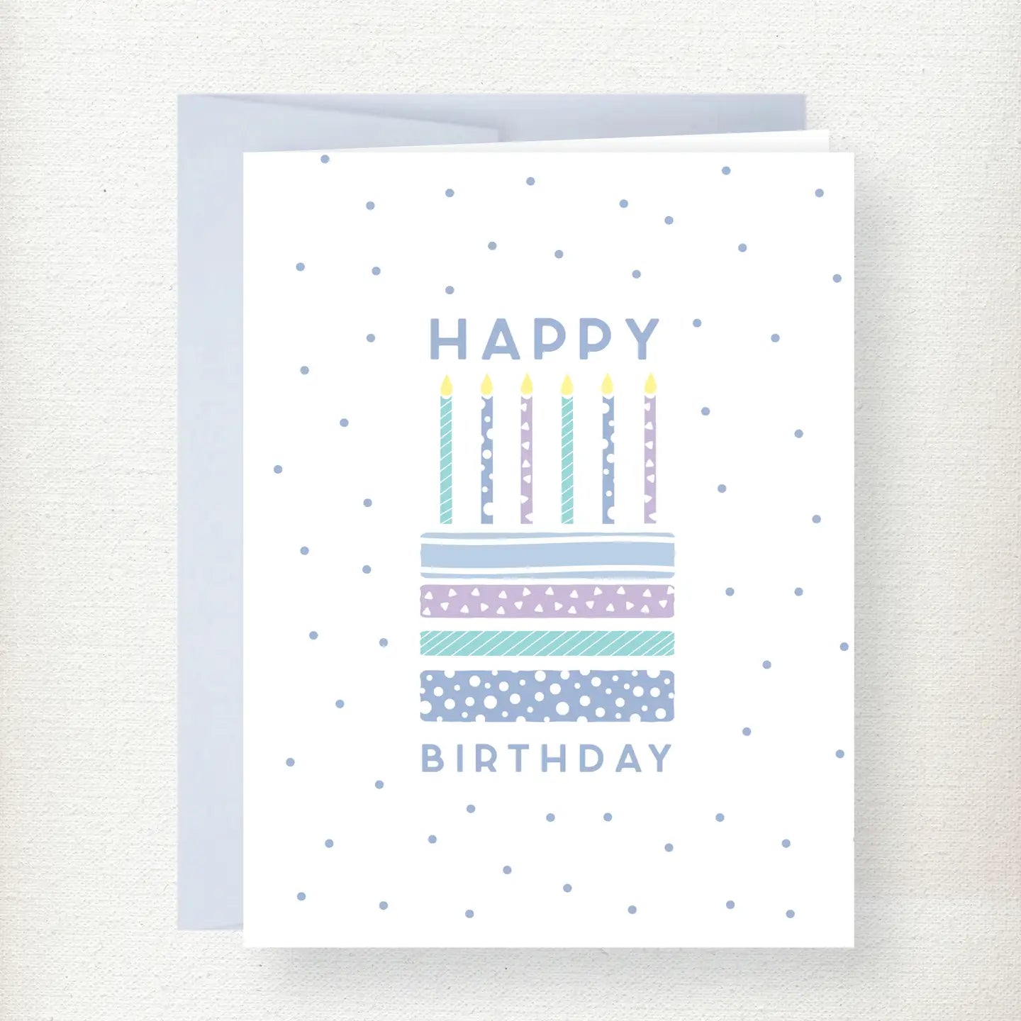 Happy Birthday greeting card featuring a colorful patterned cake with six lit candles and blue polka dot background