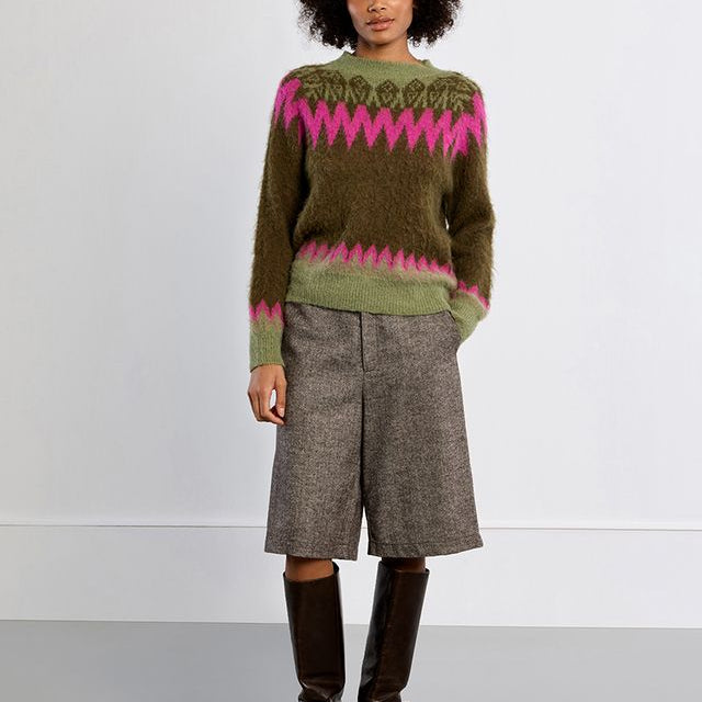 A model stands against a light gray studio background wearing a fuzzy olive green sweater with a pink and dark green Fair Isle yoke pattern, paired with gray textured knee-length shorts and dark brown knee-high boots. Main image