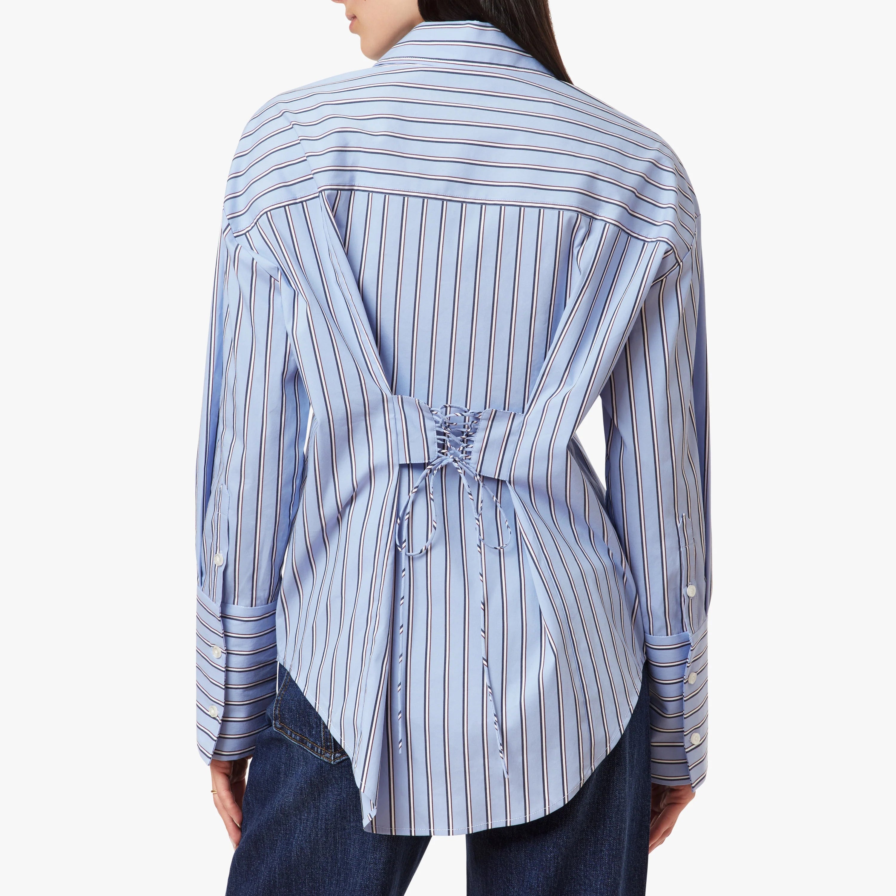 A woman shown from the back wearing a light blue and white vertically striped button-up shirt with a tie detail at the waist, paired with dark blue jeans, against a plain white background.