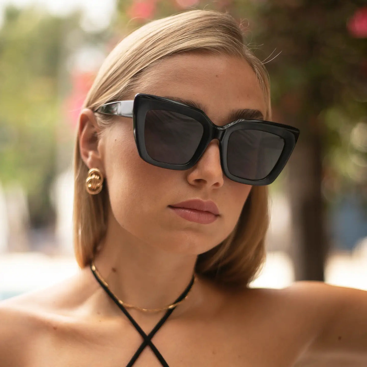 Woman wearing black Portofino sunglasses with dark lenses and white arms, paired with gold hoop earrings and a black cord