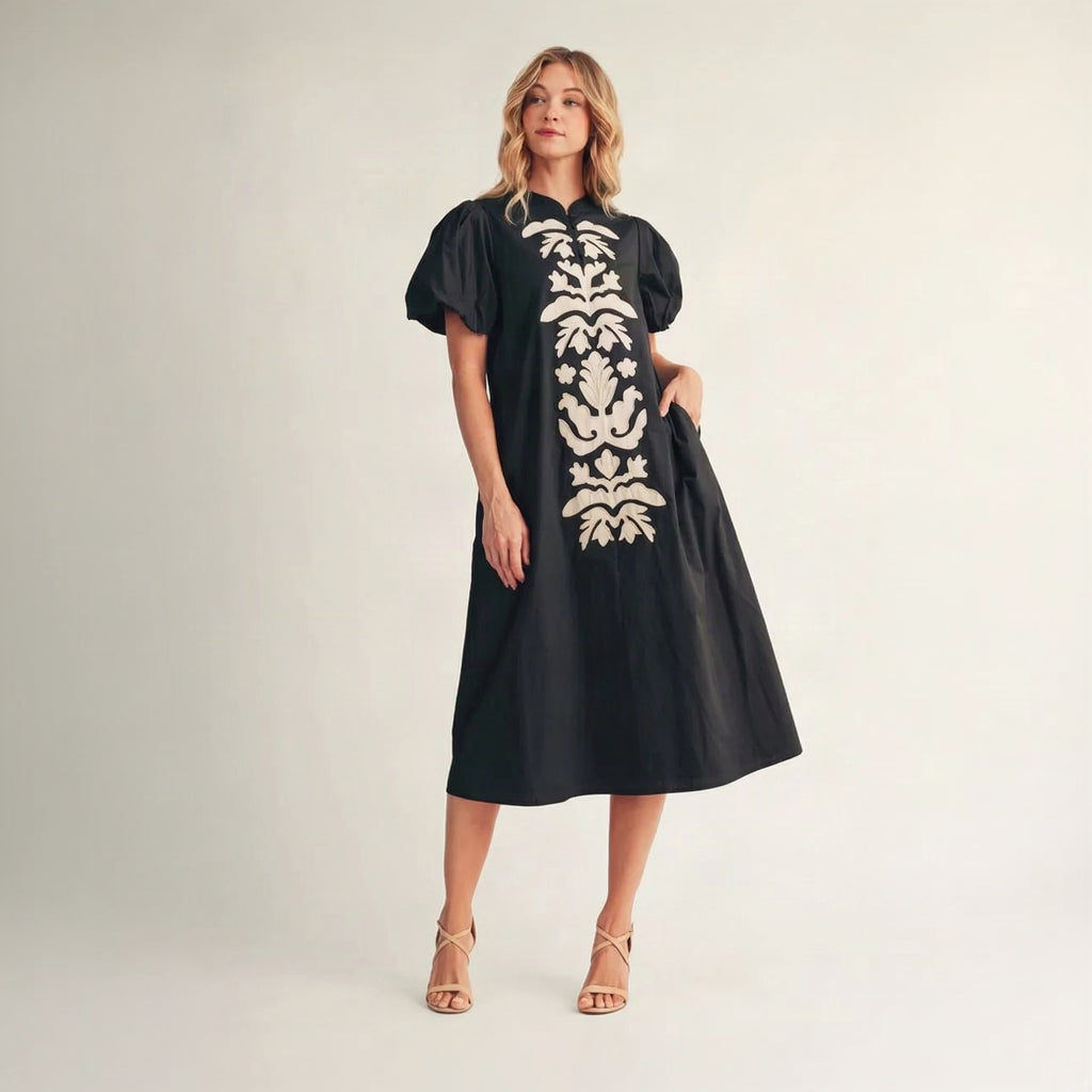 Woman wearing a black dress with white floral patterns on a plain background
