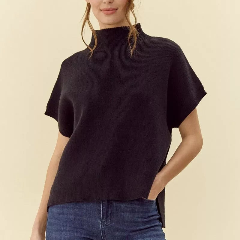 Woman wearing black ribbed mock neck short sleeve sweater paired with blue jeans, shown from chest up against cream backgrou…