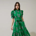 Woman wearing green Saura Floral Giles Button Up Midi dress with pink floral embroidery, puffed sleeves, and tied waist belt