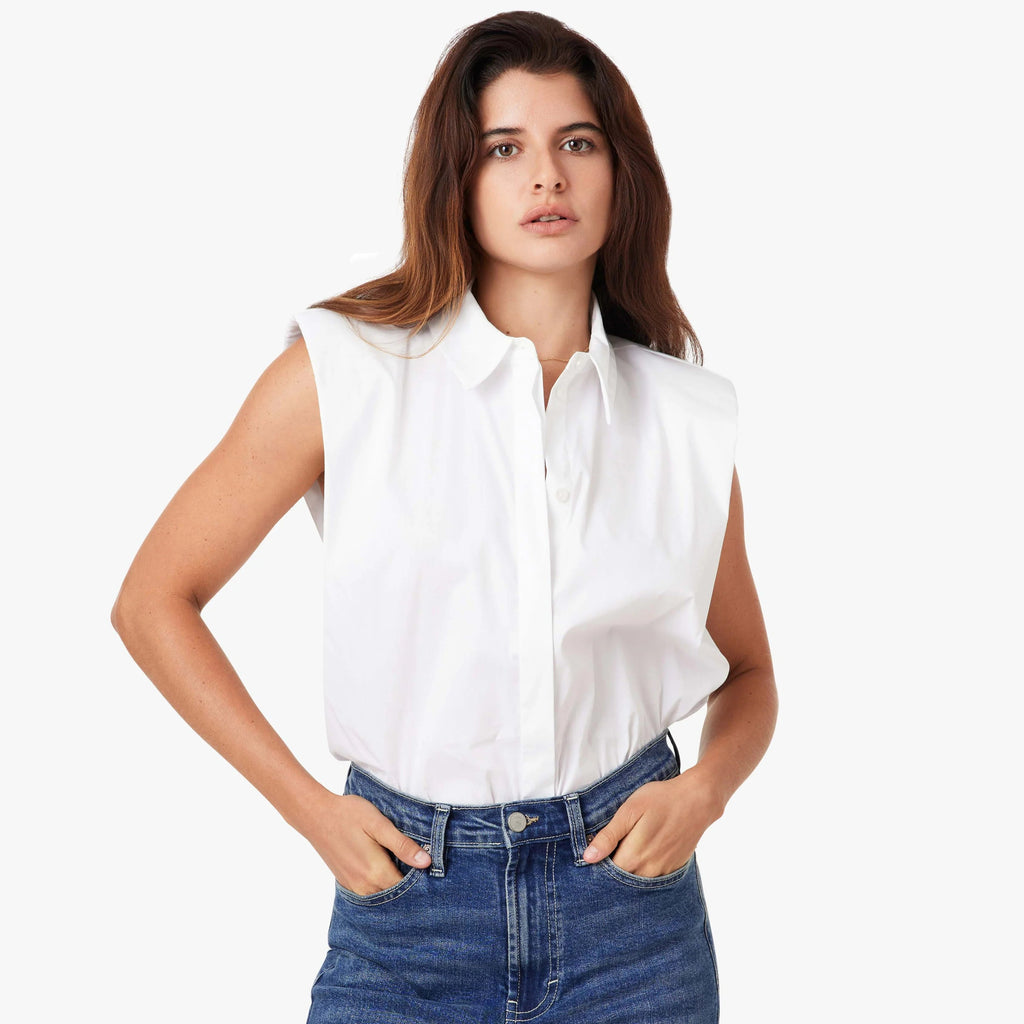 Woman wearing white sleeveless shoulder pad shirt with collar, paired with blue denim jeans