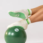 White Studio Socks with green grip dots and green stripes, worn on feet resting on a green exercise ball