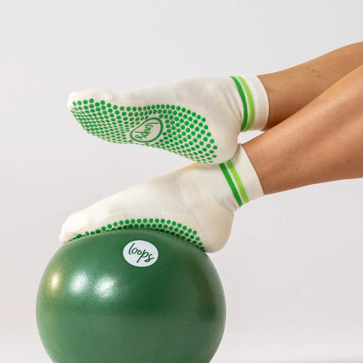 White Studio Socks with green grip dots and green stripes, worn on feet resting on a green exercise ball