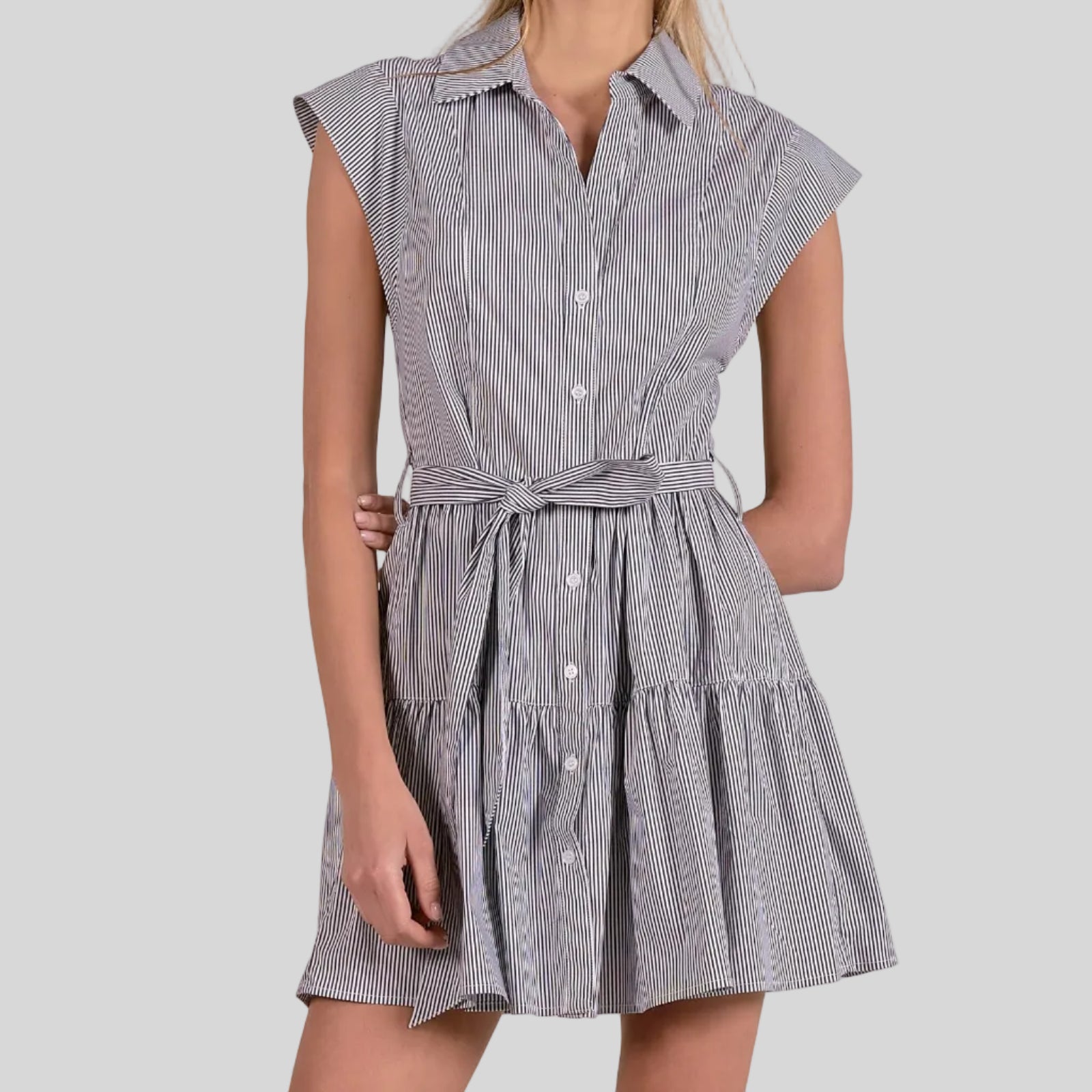 Woman wearing gray and white striped cap sleeve dress with tiered skirt and matching fabric belt