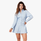 Woman wearing light blue striped mini shirt dress with long sleeves and collar, paired with hand on hip pose against white b…