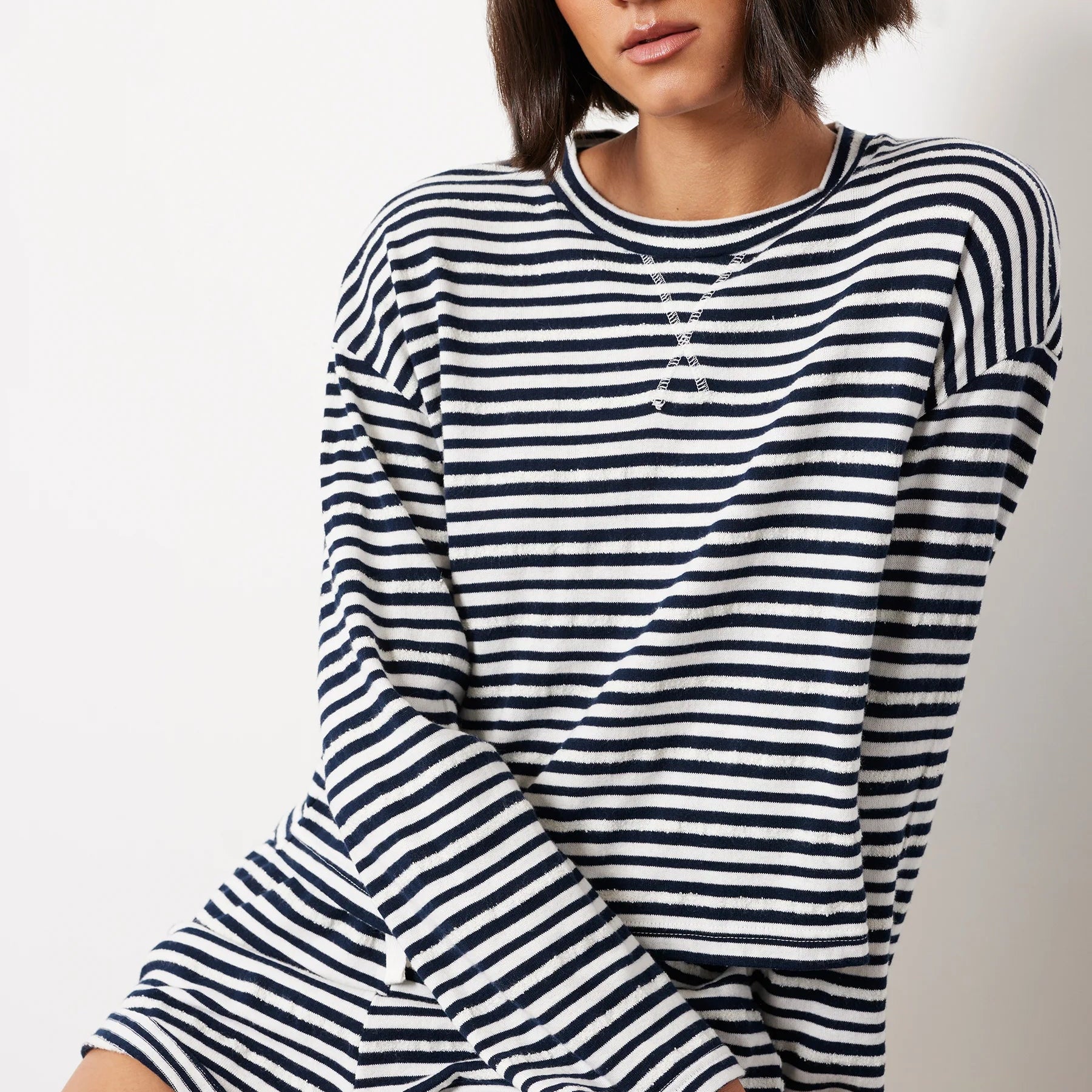 Woman wearing navy and white striped drop shoulder pullover top with long sleeves and silver chain necklace