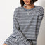 Woman wearing navy and white striped drop shoulder pullover top with long sleeves and silver chain necklace