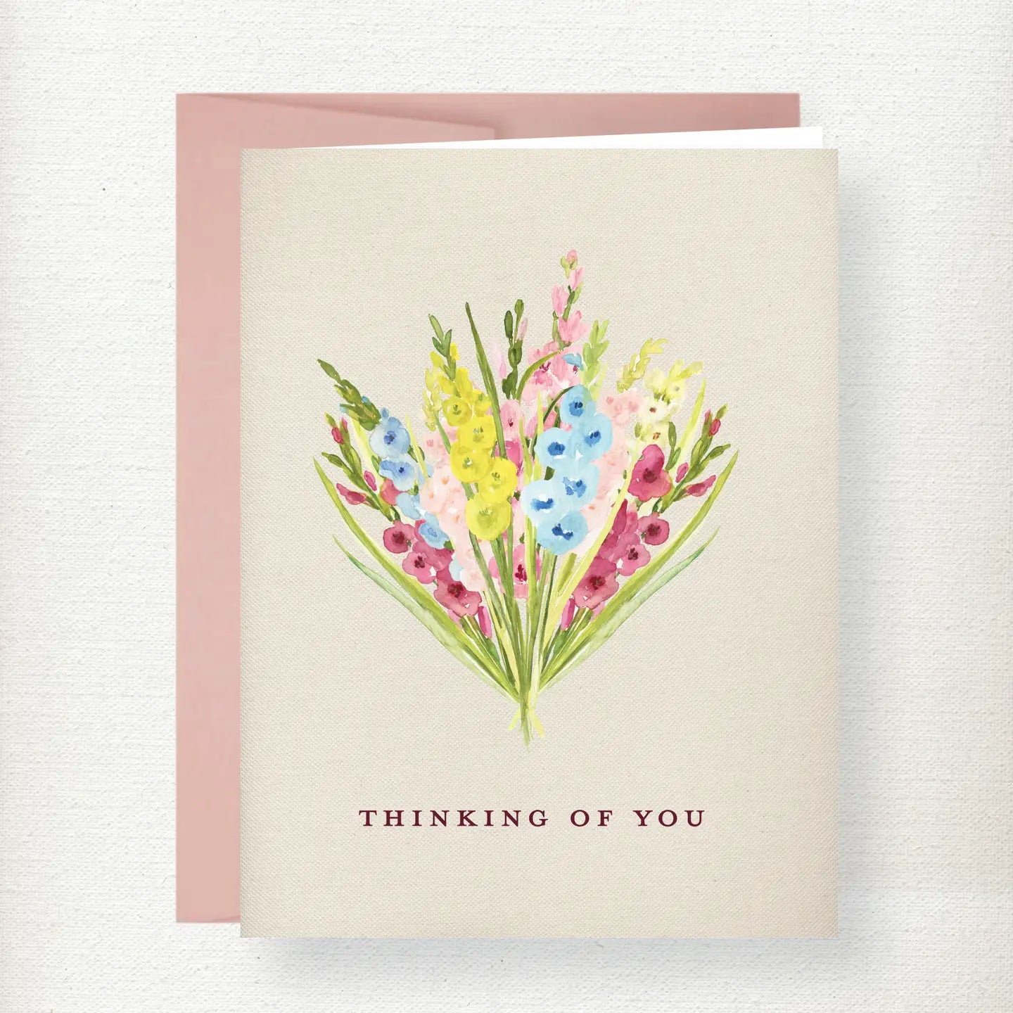Watercolor bouquet of pink, yellow, and blue gladiolus flowers with green stems on cream background with 'Thinking of You' t…