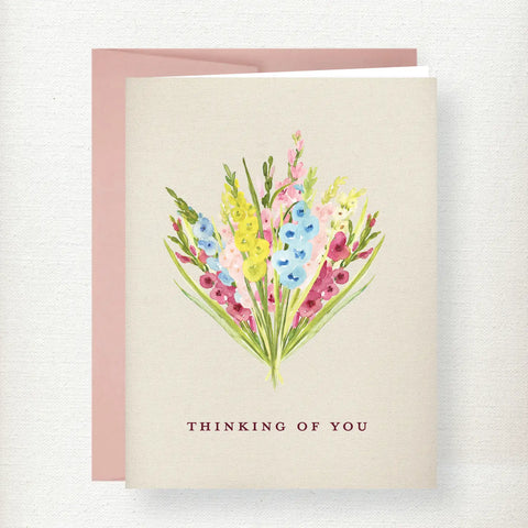 Watercolor bouquet of pink, yellow, and blue gladiolus flowers with green stems on cream background with 'Thinking of You' t…